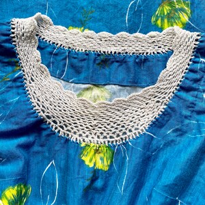 May include: A blue fabric garment with a white crocheted neckline. The fabric has a floral pattern with yellow flowers.