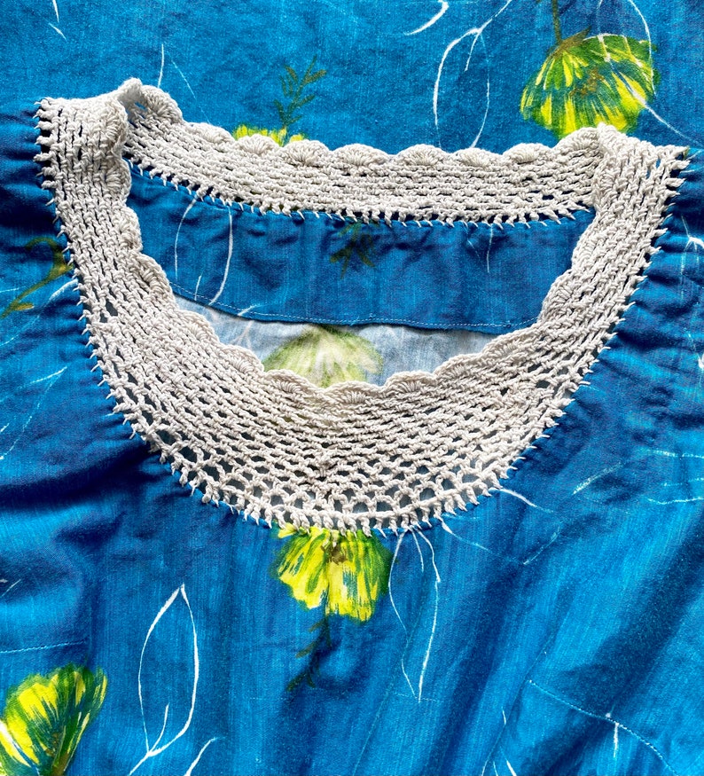 May include: A blue fabric garment with a white crocheted neckline. The fabric has a floral pattern with yellow flowers.