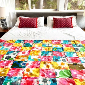 May include: A bed with a white comforter, two red decorative pillows, and a colorful patchwork quilt. The quilt features a floral pattern in shades of pink, yellow, blue, and green. Two lamps with black and white patterned bases sit on the nightstands.