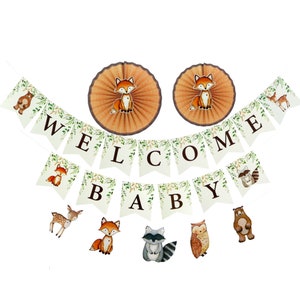 May include: A woodland themed baby shower banner with the words "Welcome Baby" in brown letters on a white background with green leaves. The banner is decorated with images of foxes, deer, raccoons, owls, and bears. There are also two paper fans with foxes on them.