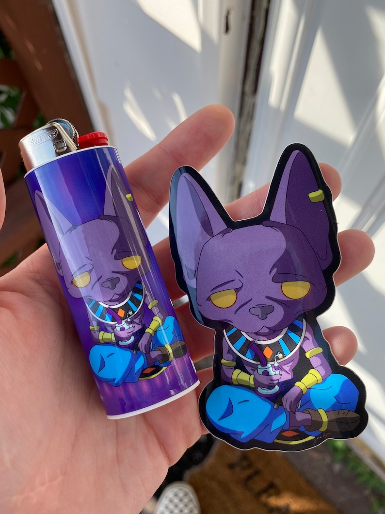 May include: A purple and blue lighter and sticker set featuring a cartoon character with yellow eyes. The lighter is a standard size, and the sticker is die-cut. The character is depicted in a seated position, holding a drink.
