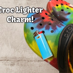 May include: A blue and yellow tie-dye Croc shoe with a blue Bic lighter charm attached. The text "Croc Lighter Charm!" is written in white letters on a gray background.