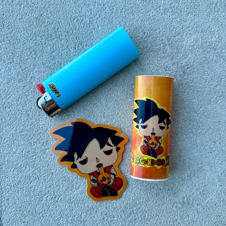 May include: A light blue BIC lighter, a sticker, and a cylindrical container. The sticker and container feature a cartoon character with black hair and red clothing, holding a smoking pipe. The container has the text "DRAGON BONG Z".