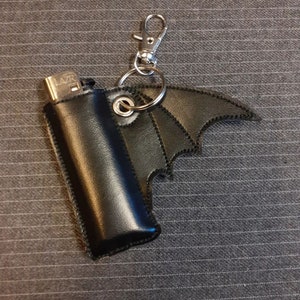 May include: Black leather keychain with a bat wing design and a silver lighter case with the word "LAZR" on it.