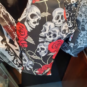 May include: Black fabric with a skull and rose pattern. The fabric is hanging from a hook. The fabric is black with white skulls and red roses.