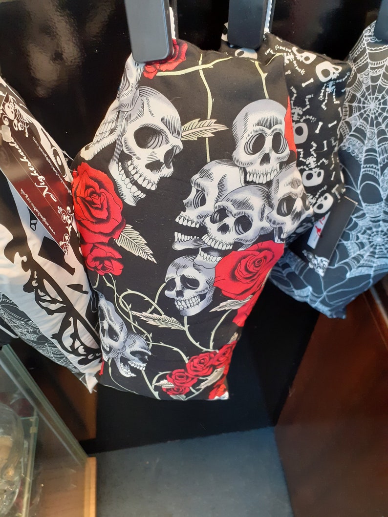 May include: Black fabric with a skull and rose pattern. The fabric is hanging from a hook. The fabric is black with white skulls and red roses.