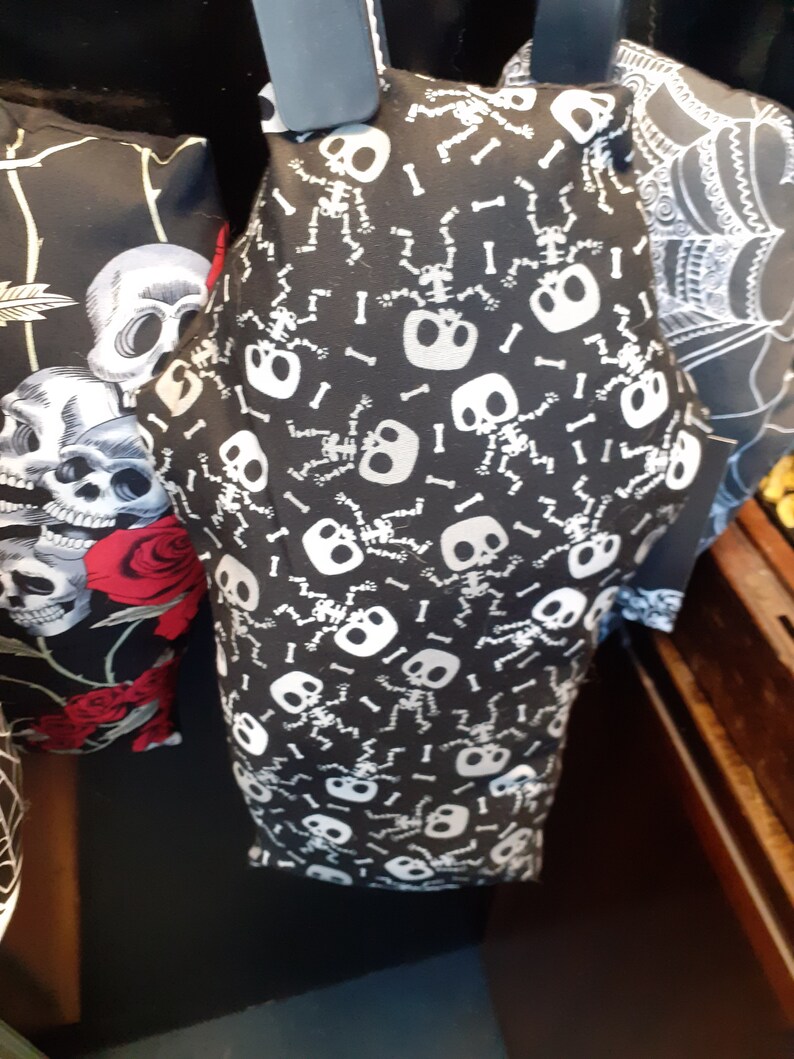 May include: Black fabric pillow with a white skeleton pattern. The skeletons are dancing and have bones scattered around them.