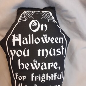 May include: Black and white coffin-shaped pillow with a spiderweb design and the text "On Halloween you must beware, for frightful things are everywhere."