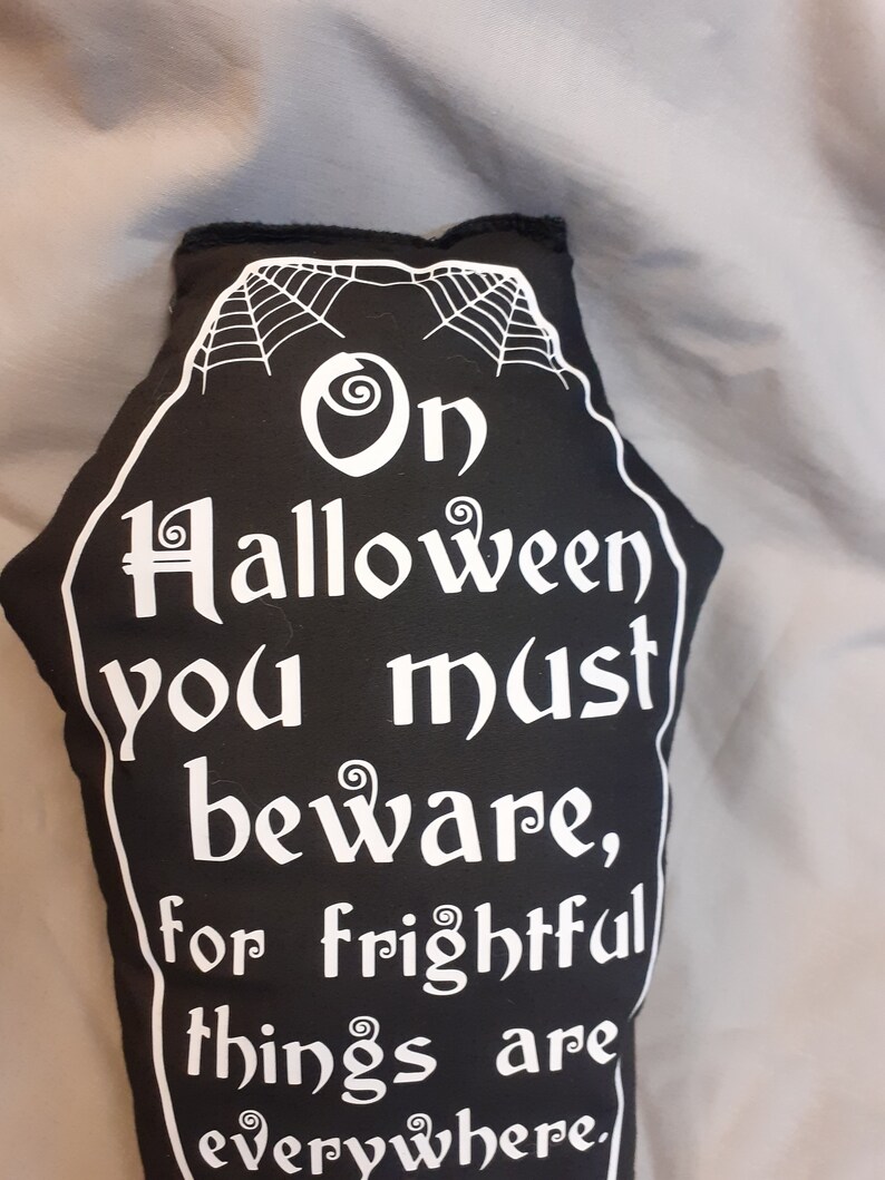 May include: Black and white coffin-shaped pillow with a spiderweb design and the text "On Halloween you must beware, for frightful things are everywhere."
