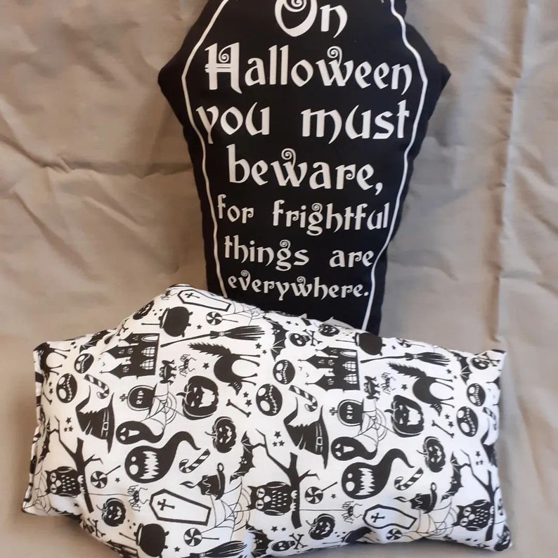 May include: Two black and white Halloween themed pillows. One pillow has a black background with white text that reads "On Halloween you must beware, for frightful things are everywhere." The other pillow has a white background with black Halloween themed illustrations.