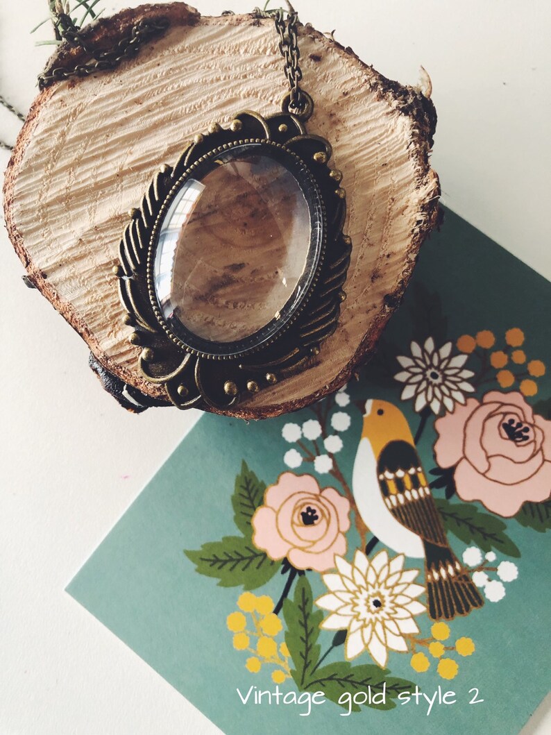 May include: A vintage gold-toned pendant necklace with a clear glass oval charm. The necklace is displayed on a wooden surface with a floral pattern background.