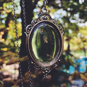 May include: A silver chain necklace with a vintage-style oval mirror pendant. The mirror has a green glass insert and an ornate silver frame.