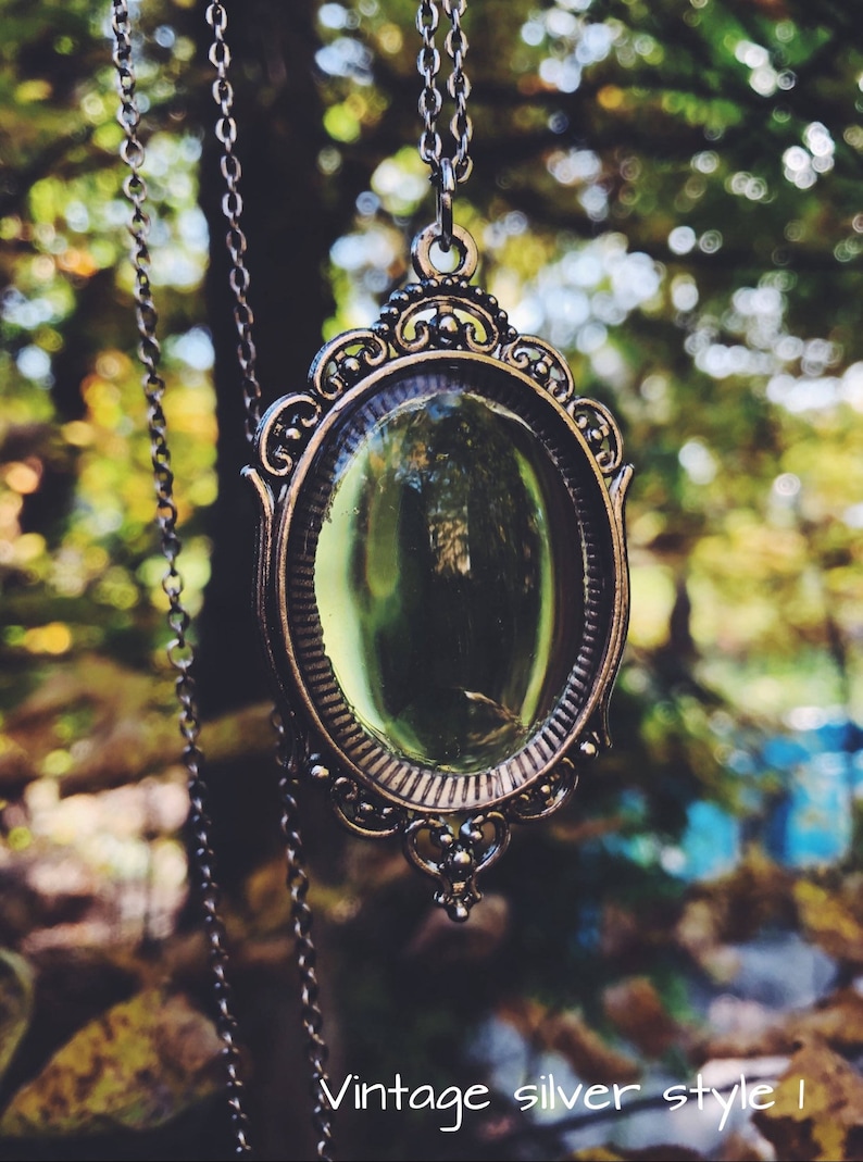 May include: A silver chain necklace with a vintage-style oval mirror pendant. The mirror has a green glass insert and an ornate silver frame.
