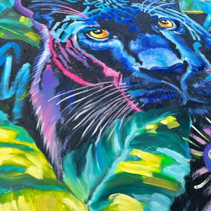 May include: A close-up of a black panther's face with bright blue and yellow eyes. The panther is surrounded by vibrant green, yellow, and blue tropical leaves.