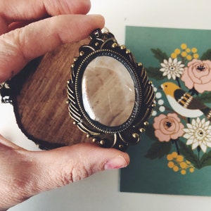 May include: A gold-toned pendant necklace with a large, clear glass oval charm set in an ornate frame. The charm has a delicate, almost invisible crack running through it.