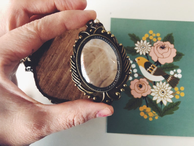 May include: A gold-toned pendant necklace with a large, clear glass oval charm set in an ornate frame. The charm has a delicate, almost invisible crack running through it.