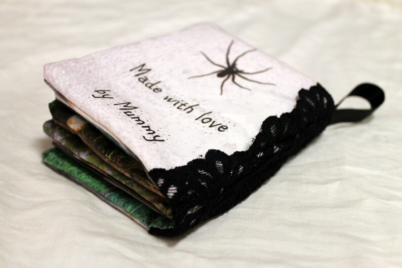 May include: A handmade book with a white cover and black lace trim. The cover has the text "Made with love by Mummy" and a black spider illustration.