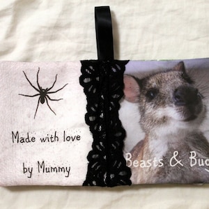 May include: A white fabric pouch with a black lace trim and a black ribbon handle. The pouch has a black spider and the text "Made with love by Mummy" on one side and a photo of a small, furry animal with the text "Beasts & Bugs" on the other side.
