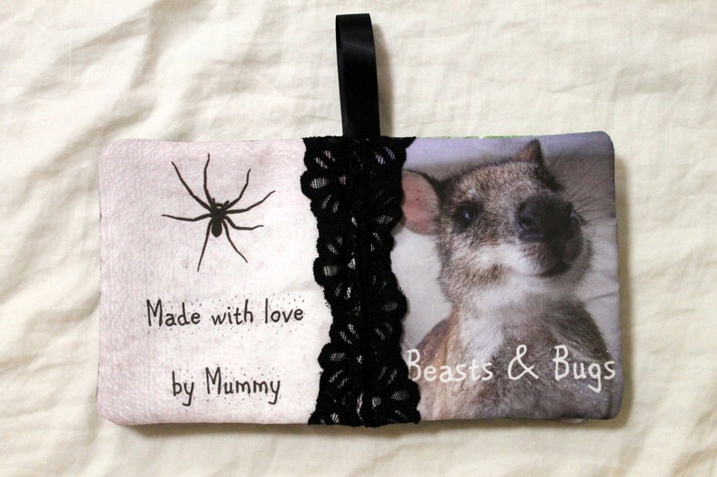 May include: A white fabric pouch with a black lace trim and a black ribbon handle. The pouch has a black spider and the text "Made with love by Mummy" on one side and a photo of a small, furry animal with the text "Beasts & Bugs" on the other side.