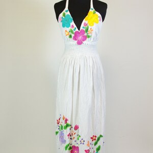 May include: White halter dress with colorful floral embroidery. The dress has a fitted bodice and a flowing skirt.