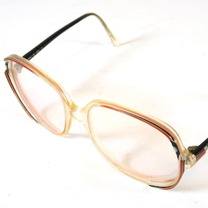 May include: Vintage eyeglasses with a clear, rectangular frame and tinted lenses. The frame features a beige and red color scheme with black arms. The glasses are set against a white background.