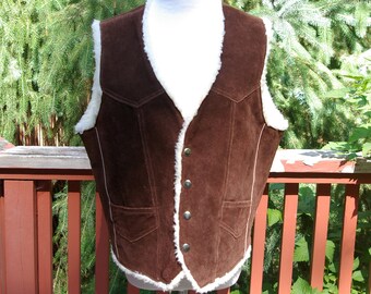 May include: A brown suede vest with a white faux fur lining. The vest has a button closure and a pocket on the front.