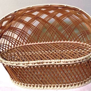 May include: A brown wicker basket with a curved back and a woven design. The basket has a white trim around the edges and a sturdy base. The basket is designed for storage or display.