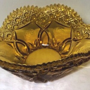 May include: Amber-coloured, decorative glass bowl with a scalloped rim and intricate geometric patterns. The bowl has a wide, shallow design with a textured surface. The bowl is likely vintage and suitable for display or serving.
