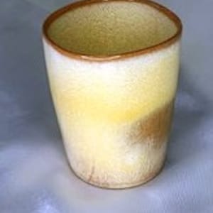 May include: A ceramic tumbler with a speckled yellow and white glaze, accented with a brown rim. The cup has a slightly irregular shape and a smooth, glossy finish. The tumbler is suitable for cold or hot beverages.