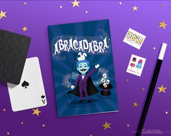 May include: A blue and purple illustrated notebook with the word "ABRACADABRA" in white letters. A cartoon magician with a white rabbit on his head is holding a wand and a top hat with playing cards coming out of it.