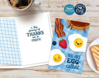 May include: A blue and white checkered card with the text "a big serving of THANKS are in ORDER!" on the inside. The front of the card features a cartoon illustration of a breakfast scene with two sunny-side-up eggs, bacon, a blueberry, a strawberry, and a pancake. The text "YOU ARE EGG-cellent" is written below the eggs.