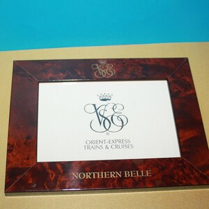 May include: A dark red wood picture frame with a gold embossed logo and the text "Orient-Express Trains & Cruises" and "Northern Belle".