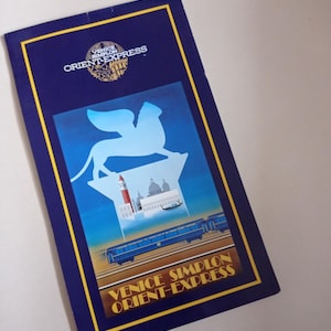 May include: A vintage travel poster for the Venice Simplon-Orient-Express train. The poster features a blue and gold color scheme with an illustration of Venice, a winged lion, and a train. The text "Venice Simplon Orient-Express" is displayed.