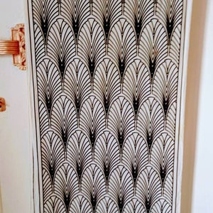 May include: An off-white scarf with a black Art Deco fan design. The scarf is hanging, displaying the full length of the pattern. The bottom border has a geometric black and white design. The scarf is made of a lightweight material.