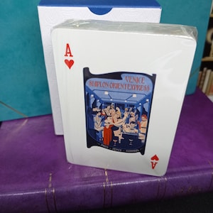Puede incluir: Una baraja de cartas con el As de corazones. El diseño de la carta incluye una ilustración del tren Simplon Orient Express con el texto "Venice" y "Paris - Venice - Istanbul". Las cartas están en una caja blanca.