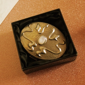 May include: A white ceramic mug with a black handle and the text "But First, Coffee" in a bold, black font. The mug is set against a blurred background, suggesting a cozy setting.