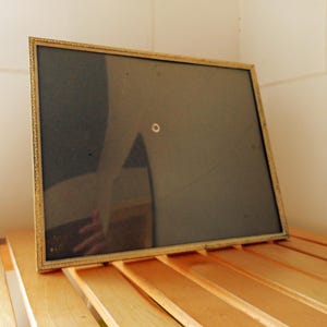 May include: A rectangular gold-colored picture frame with a decorative border. The frame has a dark backing and is resting on a wooden surface. The frame is empty and ready for a photo or artwork.