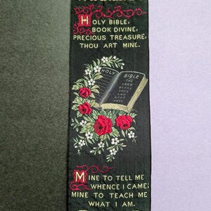 May include: Black embroidered bookmark with the text "WITH BEST WISHES." Features a floral design with red roses and white flowers, and the text "HOLY BIBLE." The bottom has a decorative design with red and white accents.