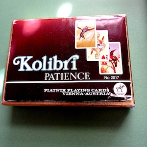 May include: A vintage card game box with the word "Kolibri" in white script above "PATIENCE". The box is dark red with gold trim and features three playing cards with bird illustrations. The text "PIATNIK PLAYING CARDS VIENNA AUSTRIA" is also visible.