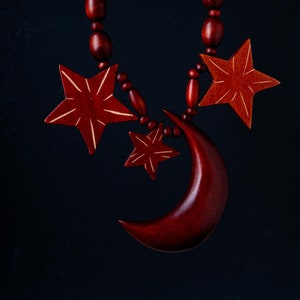 May include: A red wooden necklace with a crescent moon and three star charms. The necklace is made of round wooden beads.