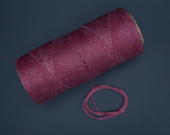 May include: A spool of deep burgundy colored waxed thread with a small length of thread unwound.