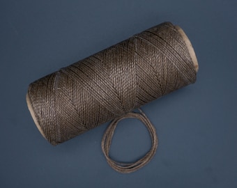May include: A spool of brown waxed thread with a small loop of thread extending from the spool.