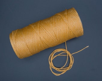 May include: A spool of golden yellow waxed thread, with a small amount of thread unwound and lying in a circle on a dark blue surface.
