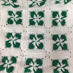 May include: A white crocheted blanket with green squares featuring a flower design.