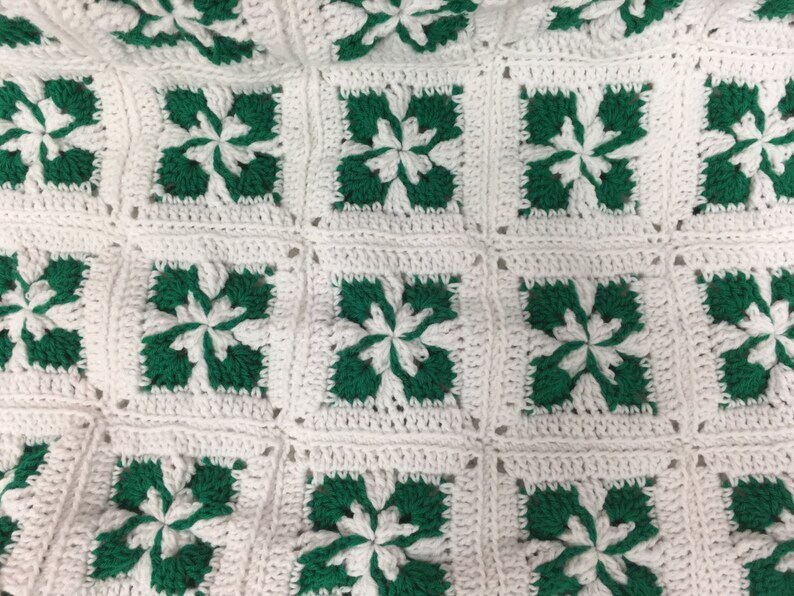 May include: A white crocheted blanket with green squares featuring a flower design.