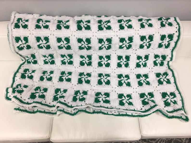 May include: A white and green crocheted blanket with a repeating pattern of four-leaf clovers. The blanket has a white background with green clovers.