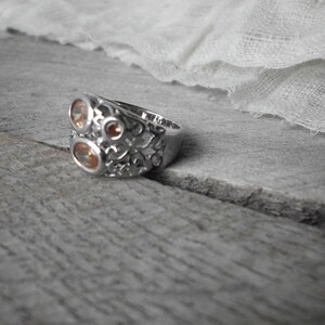 K&ouml;nnte beinhalten: Ein silberner Ring mit einem filigranen Design, das mit drei orangefarbenen Edelsteinen verziert ist.
