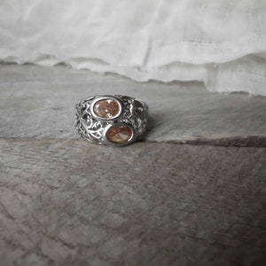 K&ouml;nnte beinhalten: Ein silberner Ring mit einem filigranen Design und zwei ovalen, orangefarbenen Edelsteinen.
