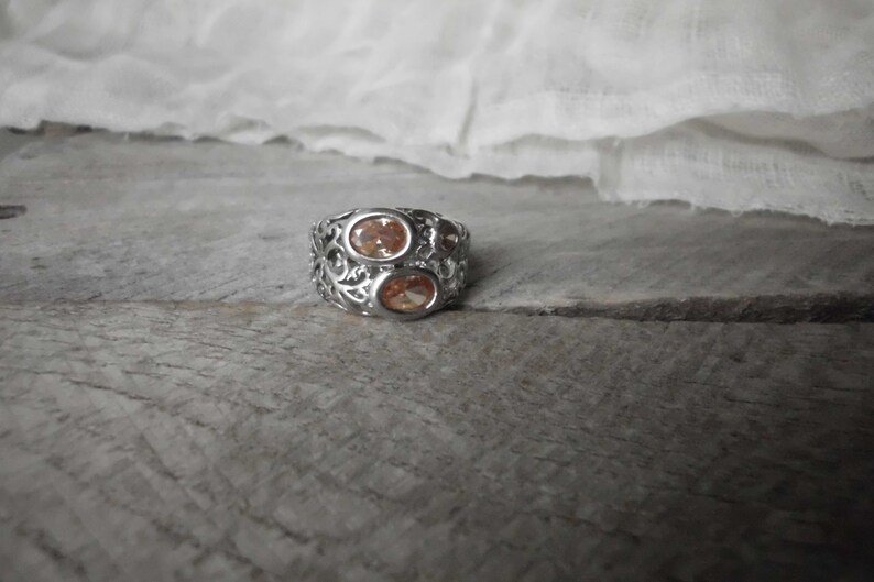 K&ouml;nnte beinhalten: Ein silberner Ring mit einem filigranen Design und zwei ovalen, orangefarbenen Edelsteinen.