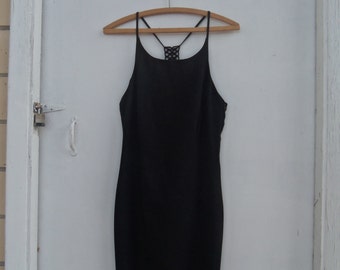 May include: A black, sleeveless dress with spaghetti straps and a decorative back detail, hanging on a wooden hanger. The dress is knee-length and appears to be made of a smooth fabric. The background is a white door.